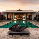 Elegant villa with a pool, stone facade, and tropical garden at sunset.